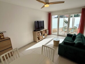 Ein Wohnzimmer mit Fernseher, einer Couch, einem Esstisch und einem Balkon mit Gartenmöbeln.