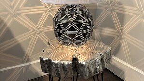 A modern lamp with a geometric pattern on a wooden stand with metal legs, placed on a wooden floor.