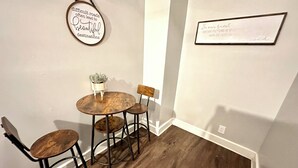 A dining area with a round wooden table, two chairs, a potted plant, and two wall decorations.