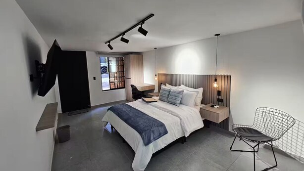 A modern bedroom with a bed, bedside tables, a chair, and a TV mounted on the wall. - Naranjo Cozy Loft w/AC in Laureles (Medellín)