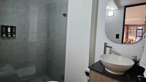 A modern bathroom with a glass-enclosed shower, a white toilet, and a vanity with a sink and mirror. - Naranjo Cozy Loft w/AC in Laureles (Medellín)