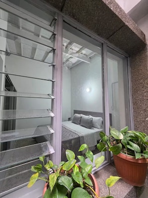 A bedroom with a bed, a nightstand, and a window with blinds. There are potted plants on the windowsill. - San Joaquin House 5BR in Laureles (Medellín)