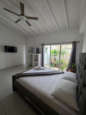 A modern bedroom with a bed, a ceiling fan, a TV, a small kitchenette, and a sliding glass door to a balcony. - Fiorentina Big House 8BR in Laureles (Medellín)