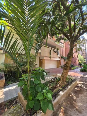 A residential building with a garage, surrounded by lush greenery and a paved walkway. - Fiorentina Big House 8BR in Laureles (Medellín)