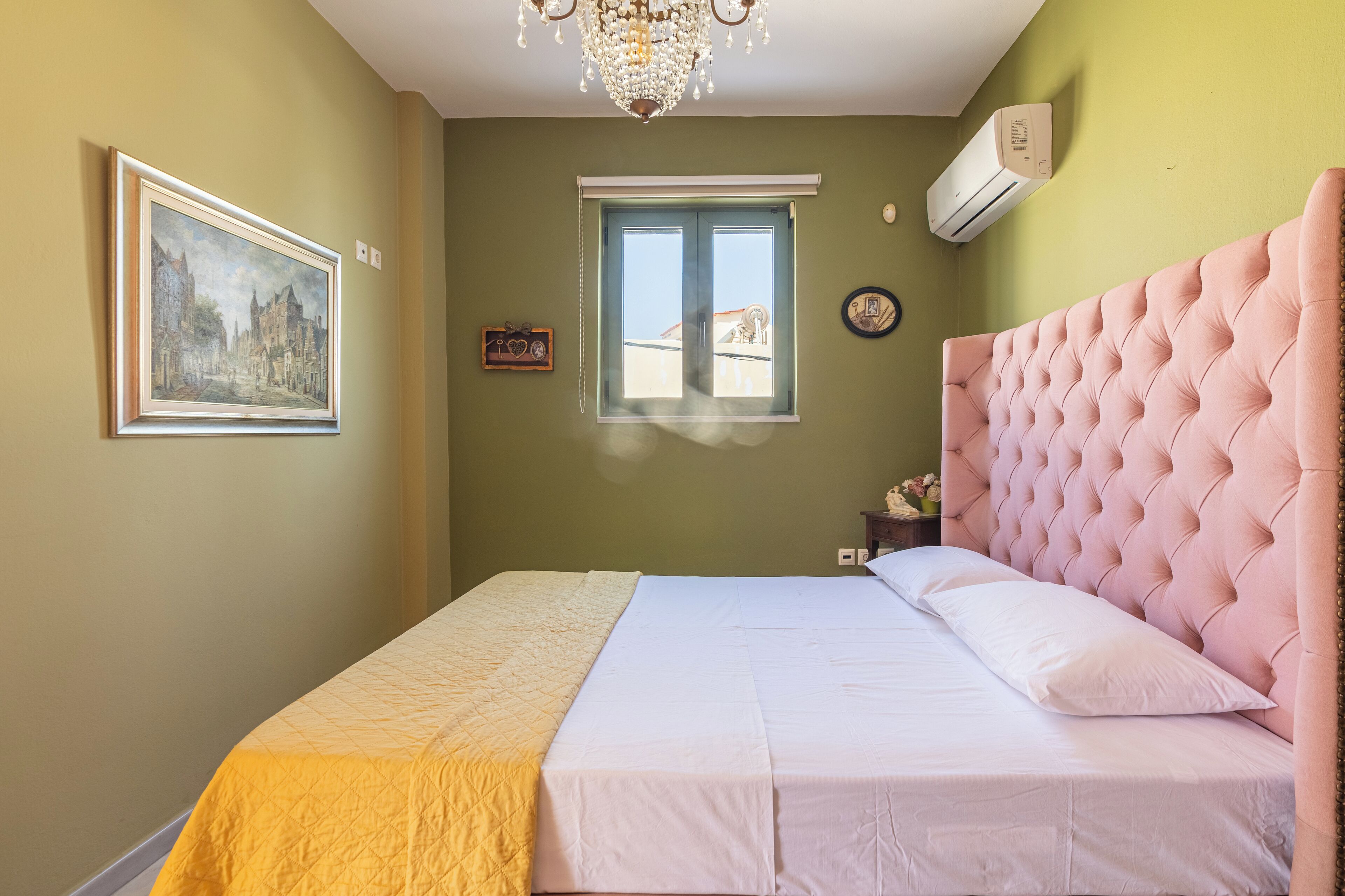 A bedroom with a bed, a window, a chandelier, and a wall-mounted air conditioner.