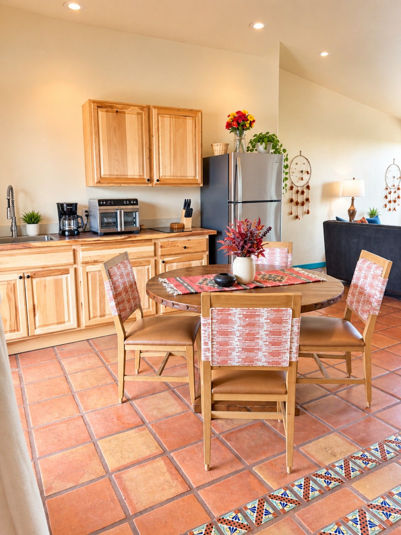 A kitchen with wooden cabinets, a refrigerator, a coffee maker, and a dining area with a round table and chairs.