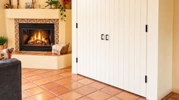A living room with a fireplace, a large white wardrobe, and a patterned tile floor.
