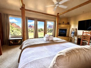 A bedroom with a large bed, a ceiling fan, a television, and a view of red rock formations.