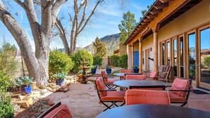 An outdoor patio with tables and chairs, surrounded by potted plants and a large tree.