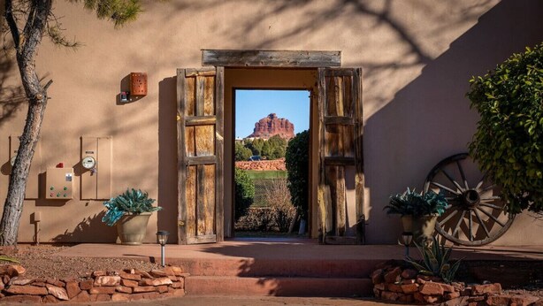 A rustic entrance with a wooden door, a stone wall, and a view of a red rock formation.