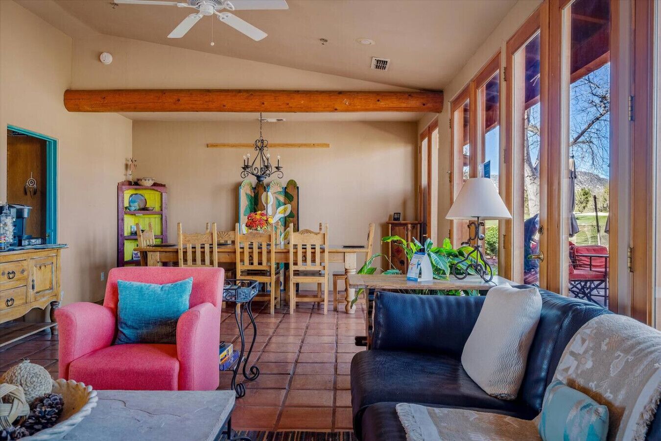 Amplia sala de estar con techo alto, vigas de madera, comedor con sillas de madera, un sofá y una mesa con lámpara.