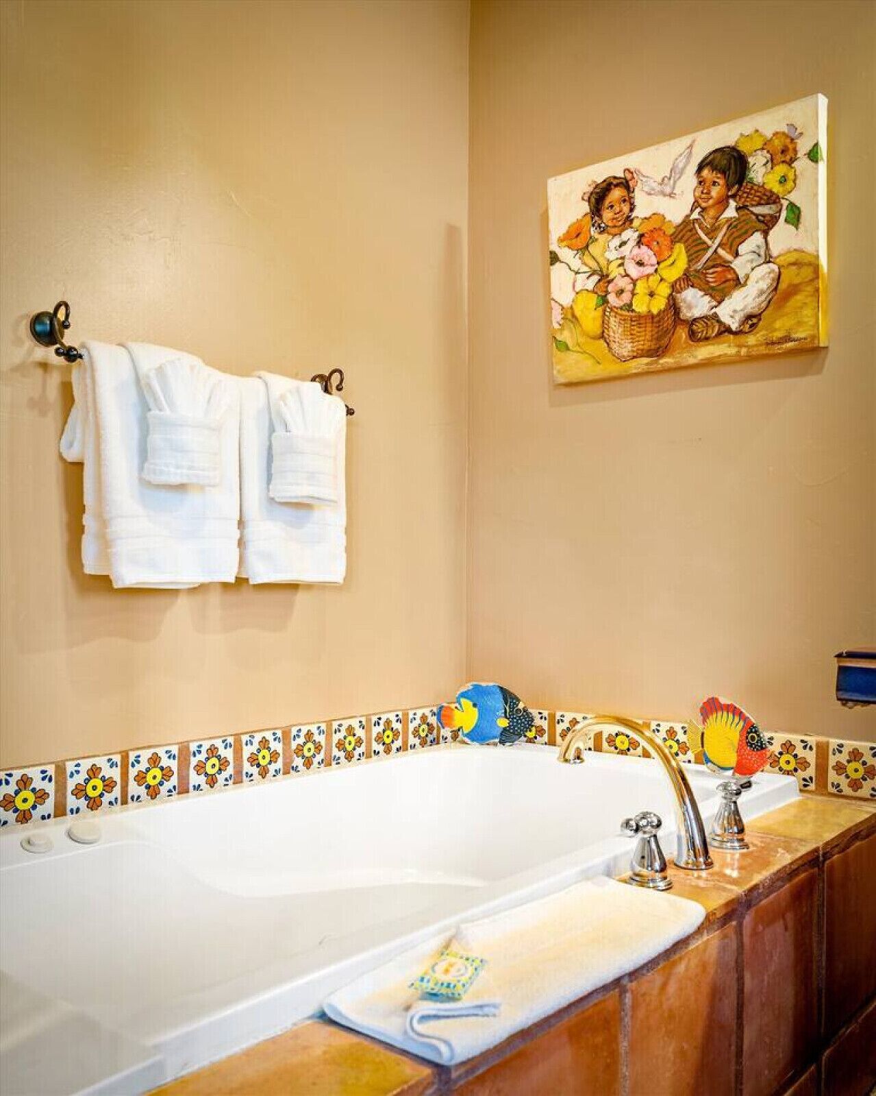 A bathroom with a bathtub, a towel rack with two towels, a painting of children with flowers, and a tiled border.