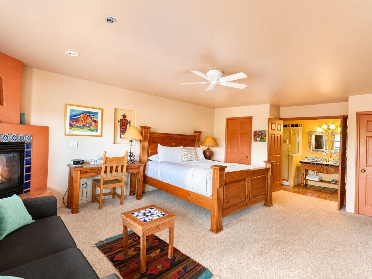 A bedroom with a bed, a desk, a chair, a television, and a bathroom with a mirror and sink.