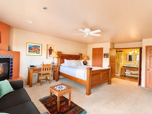 A bedroom with a bed, a desk, a chair, a television, and a bathroom with a mirror and sink.
