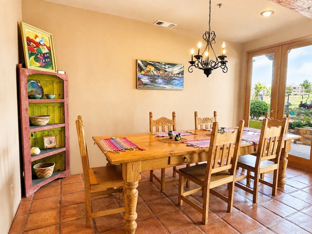 A dining area with a wooden table and chairs, a chandelier, and a view through a glass door.