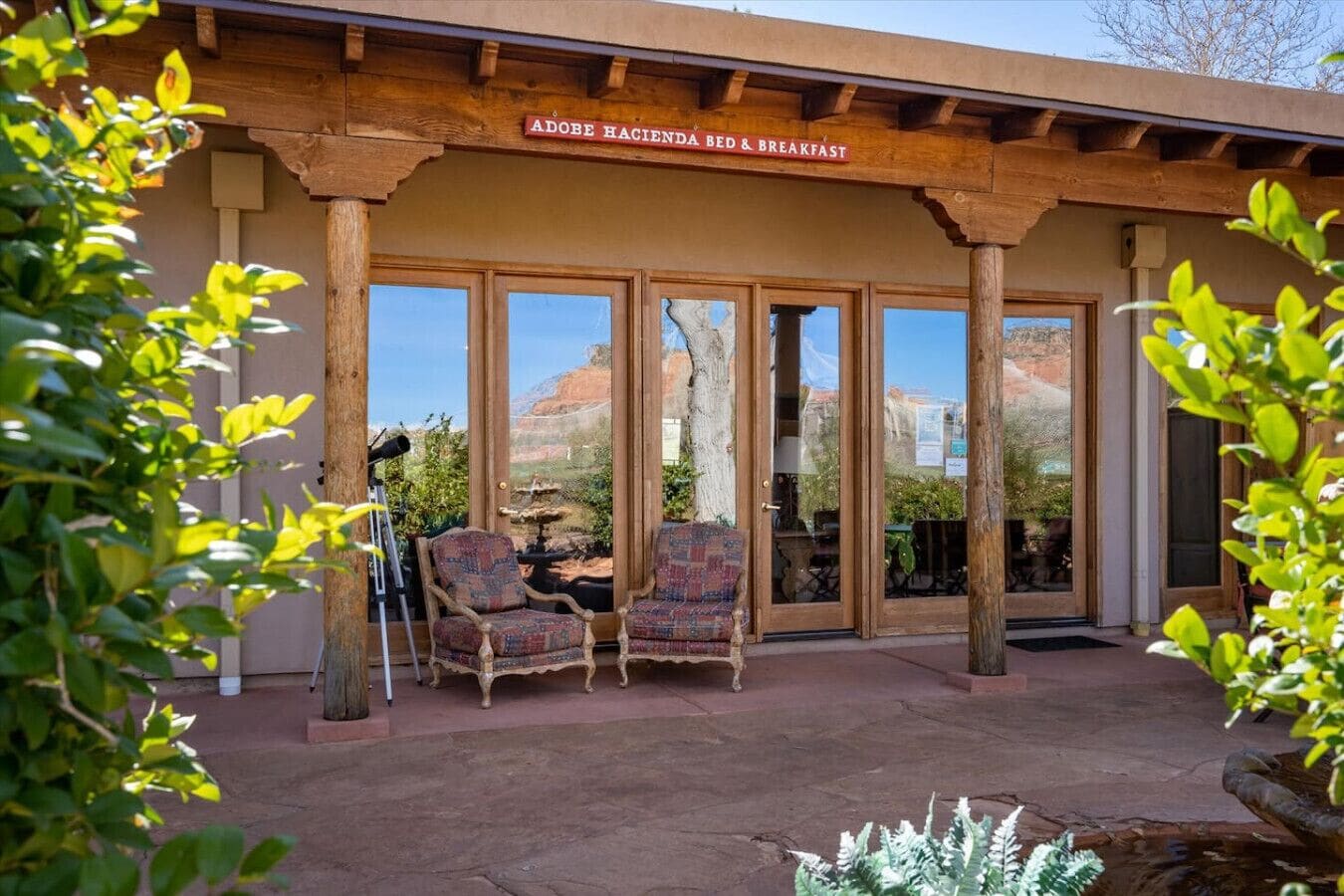 Una pérgola de madera con un letrero que dice "Adobe Hacienda Bed & Breakfast" y dos sillas con diseños debajo.