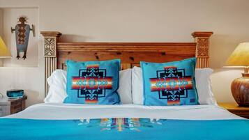 Una cama con dos almohadones decorativos, un cabecero de madera y una mesita de noche con una lámpara.