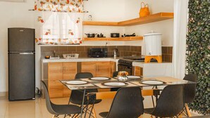 A compact kitchen with a central island, a refrigerator, and a dining area with chairs and a table set for four. - Casa con la mejor ubicación a minutos de Xetulul (Santa Cruz Muluá)