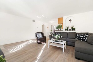 A modern living room with a leather armchair, a sofa, a coffee table, and a cross on the wall.