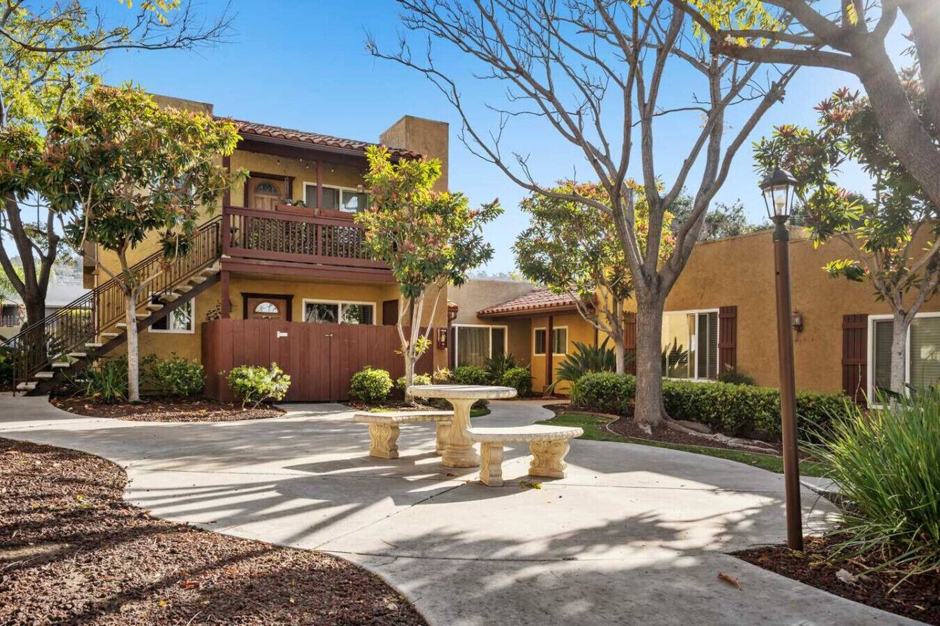 A residential area with a two-story building, a staircase, and a courtyard with a stone bench.
