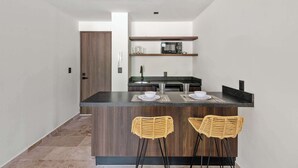 Una cocina moderna con una isla central, dos taburetes de bar y un microondas en un estante.