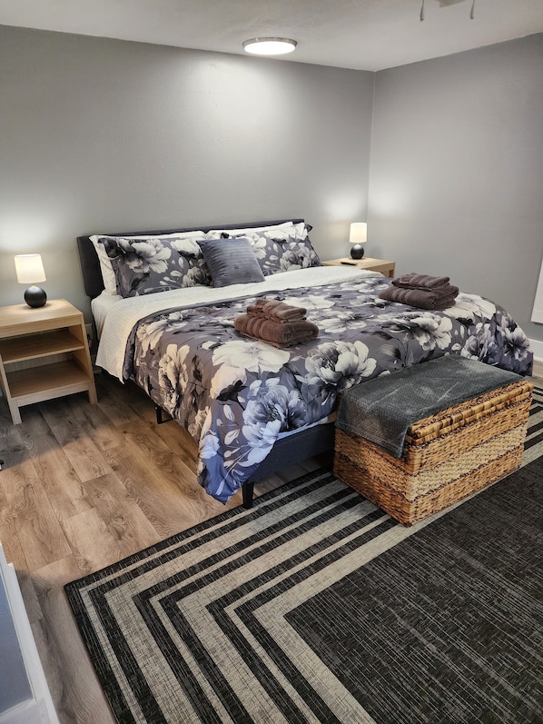 A neatly arranged bedroom with a bed, bedside tables, a bedside lamp, a woven basket, and a patterned rug.