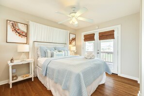 Ein Schlafzimmer mit Bett, Deckenventilator, Nachttisch, Lampe und einer Tür mit Blick.
