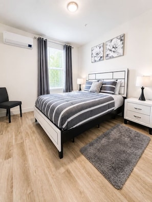 Une chambre à coucher avec un lit, des tables de chevet, une chaise, un tapis et des œuvres d’art accrochées au mur.