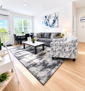 A modern living room with a sofa, armchair, coffee table, and a painting on the wall. - Stylish 1st-Floor Suite Near Convention Center (Hot Springs)