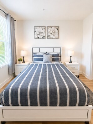 A bedroom with a bed, two bedside tables, a nightstand, a window with curtains, and two wall-mounted flower paintings. - Stylish 1st-Floor Suite Near Convention Center (Hot Springs)