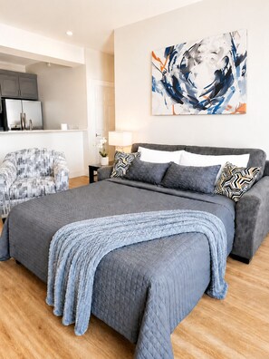 A modern bedroom with a large bed, a grey sofa, a TV, and abstract art on the wall. - Stylish 1st-Floor Suite Near Convention Center (Hot Springs)