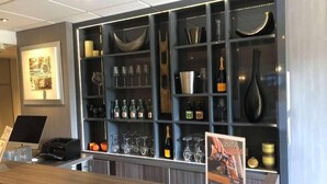 A bar area with shelves of bottles, glasses, and a poster. - Ibis Styles Saint Quentin (Saint-Quentin)