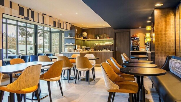 A modern restaurant with a bar area, seating arrangements, and a view through large windows. - Ibis Styles Saint Quentin (Saint-Quentin)