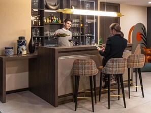 A bar area with a bartender, a customer, and three patterned stools. - Kyriad Saint Quentin (Saint-Quentin)