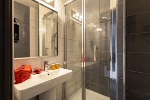 Une salle de bain moderne avec une douche à l’italienne en verre, un lavabo blanc et un grand miroir.