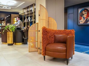 A modern lobby with a reception desk, a seating area with a fur-covered chair, and a decorative wall with a painting. - Kyriad Saint Quentin (Saint-Quentin)