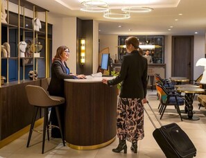 A reception area with a counter, a computer, and a seating area with tables and chairs. - Kyriad Saint Quentin (Saint-Quentin)