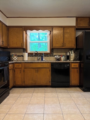 A kitchen with wooden cabinets, a window with a view of trees, a sink, and a dishwasher.