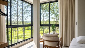 A hotel room with large windows, a bed, a chair, and a small table with a plant. - Pousada Casa Decore (Capitólio)