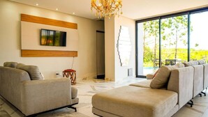 A modern living room with a sofa set, a mounted TV, and a chandelier. - Pousada Casa Decore (Capitólio)