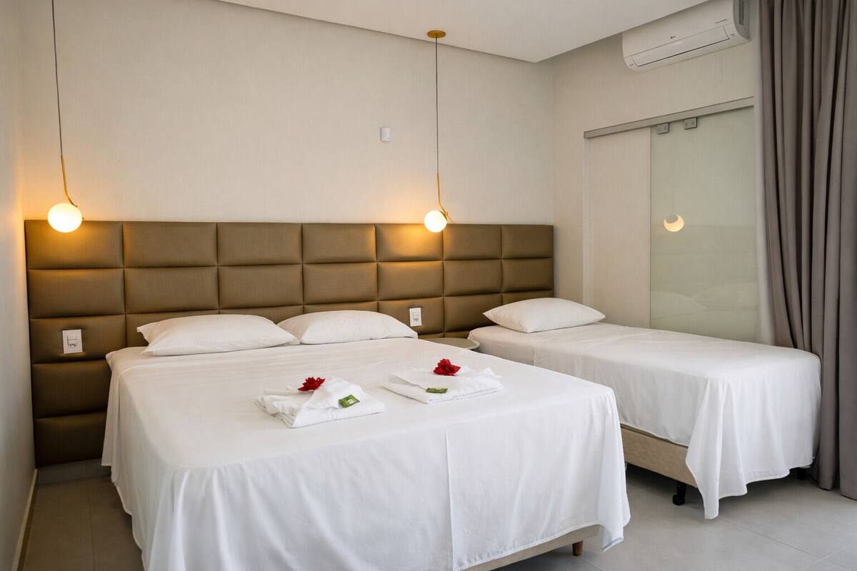 A hotel room with two beds, a padded headboard, bedside lamps, and a window with curtains.
