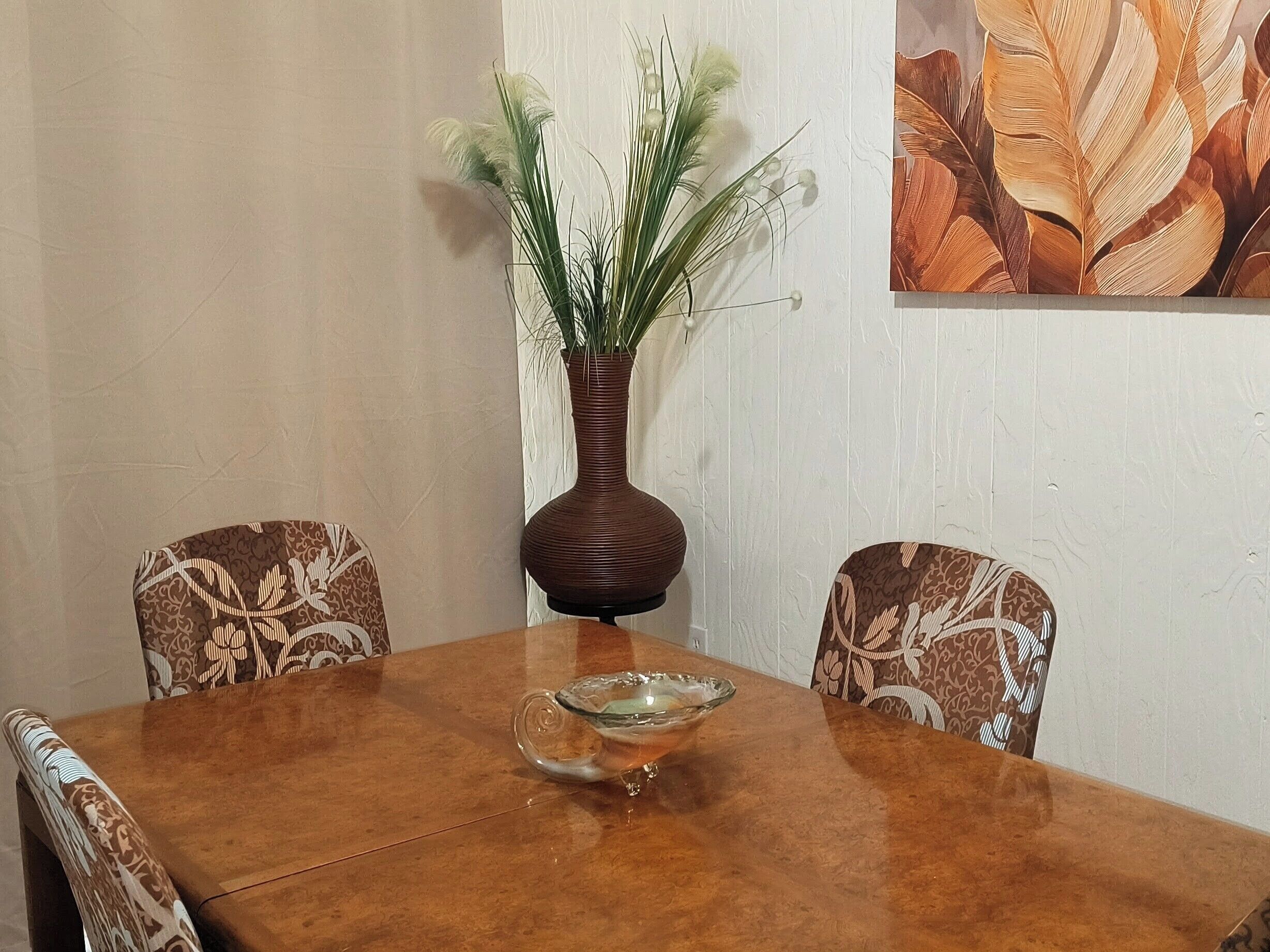 Spisebord med en vase med planter, to mønstrede stole og en dekorativ skål.