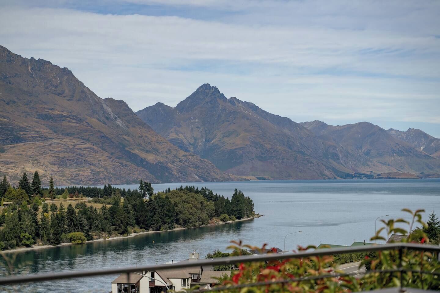 Un lac avec des montagnes en arrière-plan, et une vue sur une maison dotée d’un balcon surplombant l’eau.