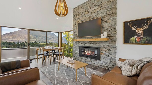 A modern living room with a stone fireplace, a flat-screen TV, and a dining area with a mountain view. - Earnslaw Lakeview Retreat, close to town + parking (Queenstown)