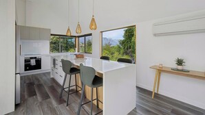 A modern kitchen with a central island, bar stools, pendant lighting, and a view of greenery. - Earnslaw Lakeview Retreat, close to town + parking (Queenstown)