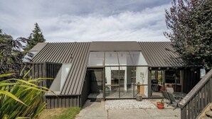 A modern house with a sloped roof, large glass doors, and a small patio area with outdoor seating. - Earnslaw Lakeview Retreat, close to town + parking (Queenstown)