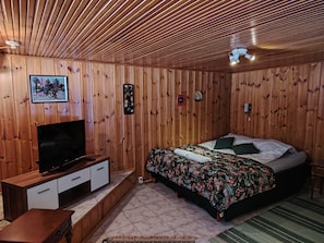 Ein Zimmer mit Holzwänden, einem Bett, einem Fernseher auf einer Holzkommode und einem Deckenventilator.