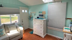 A room with a ceiling fan, a window with blinds, a desk with a lamp, a dresser, and a couch. - Charming 1-bedroom cottage in York perfect for a relaxing getaway. (York)
