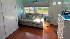 A room with a ceiling fan, a sofa with pillows, a dresser, and a door with a window. - Charming 1-bedroom cottage in York perfect for a relaxing getaway. (York)