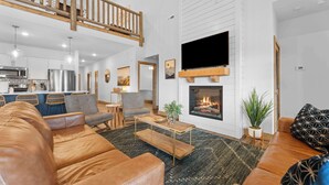 Una sala de estar moderna con chimenea, sofá de cuero, mesa de centro de madera y televisor montado en la pared.